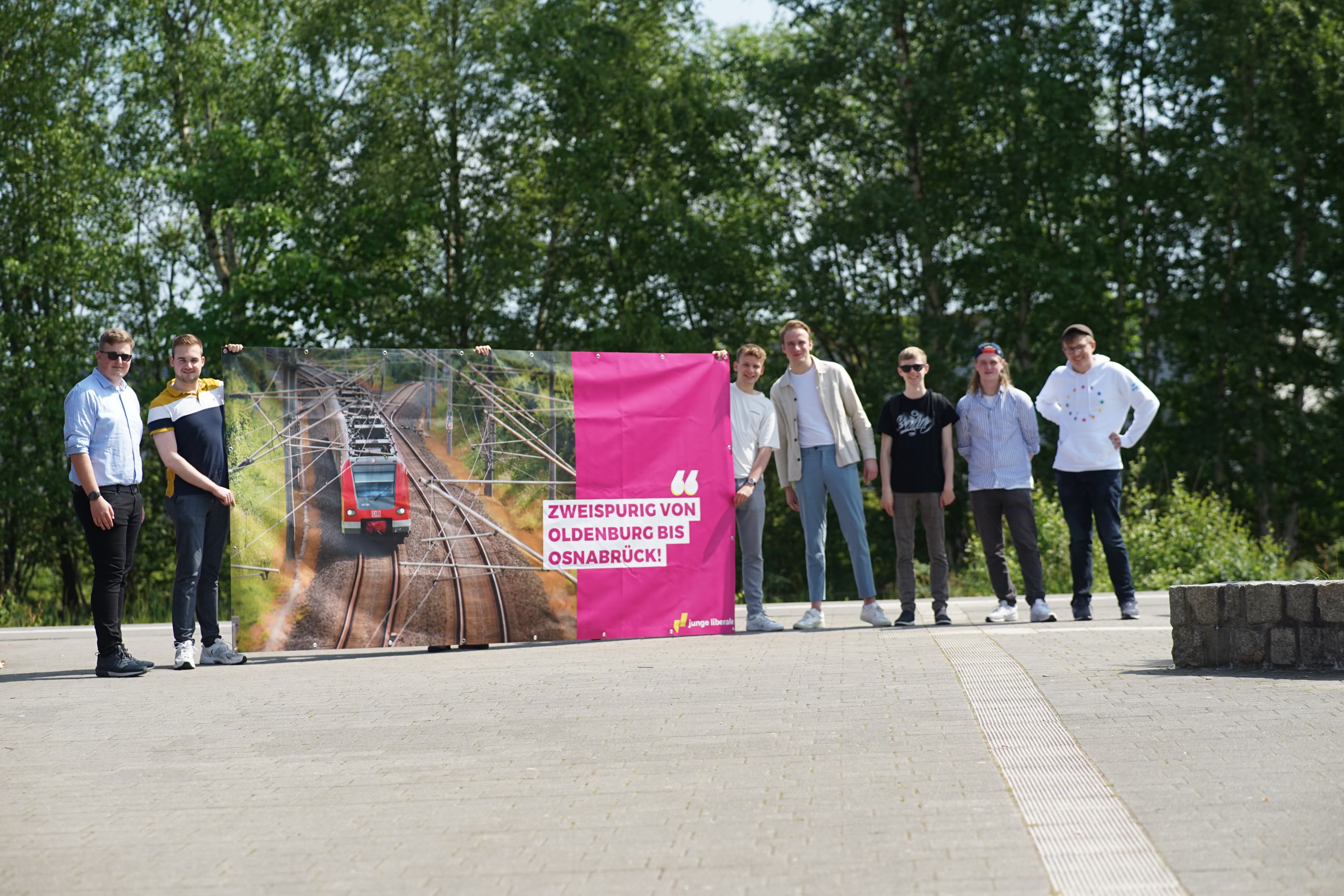 Die Jungliberalen halten das Plakat für den zweispurigen, vollelektrifizierten Ausbau am Bahnhof in Cloppenburg hoch