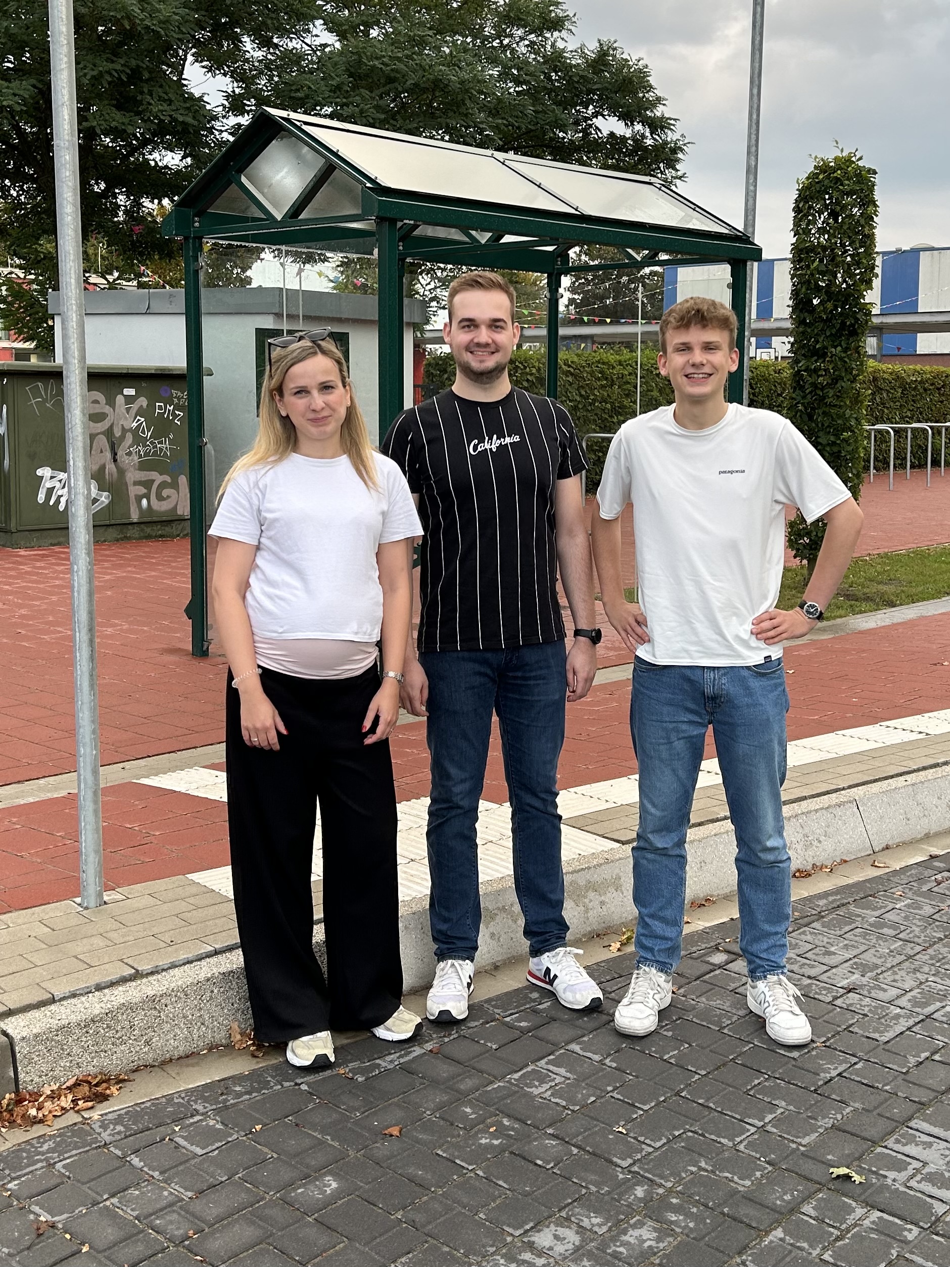 Carolin Abeln, Oliver Renze und Paul Lanwer stehen vor der Bushaltestelle einer Schule