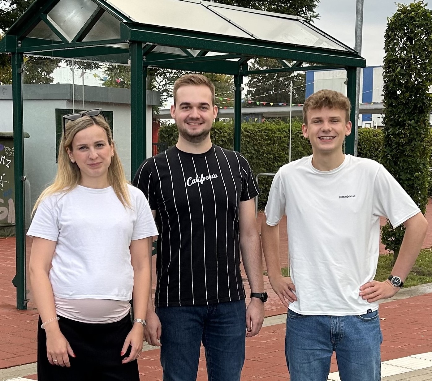 Carolin Abeln, Oliver Renze und Paul Lanwer stehen vor einer Bushaltestelle einer Schule