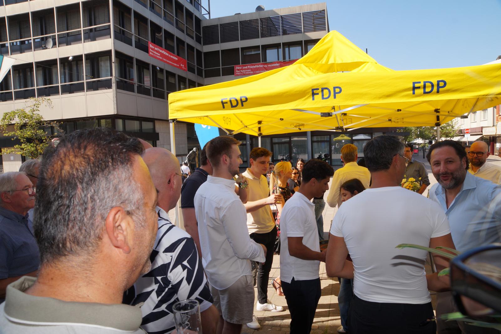 Gäste versammeln sich bei sommerlichem Wetter unter dem gelben FDP-Pavillon vor der Kreisgeschäftsstelle.