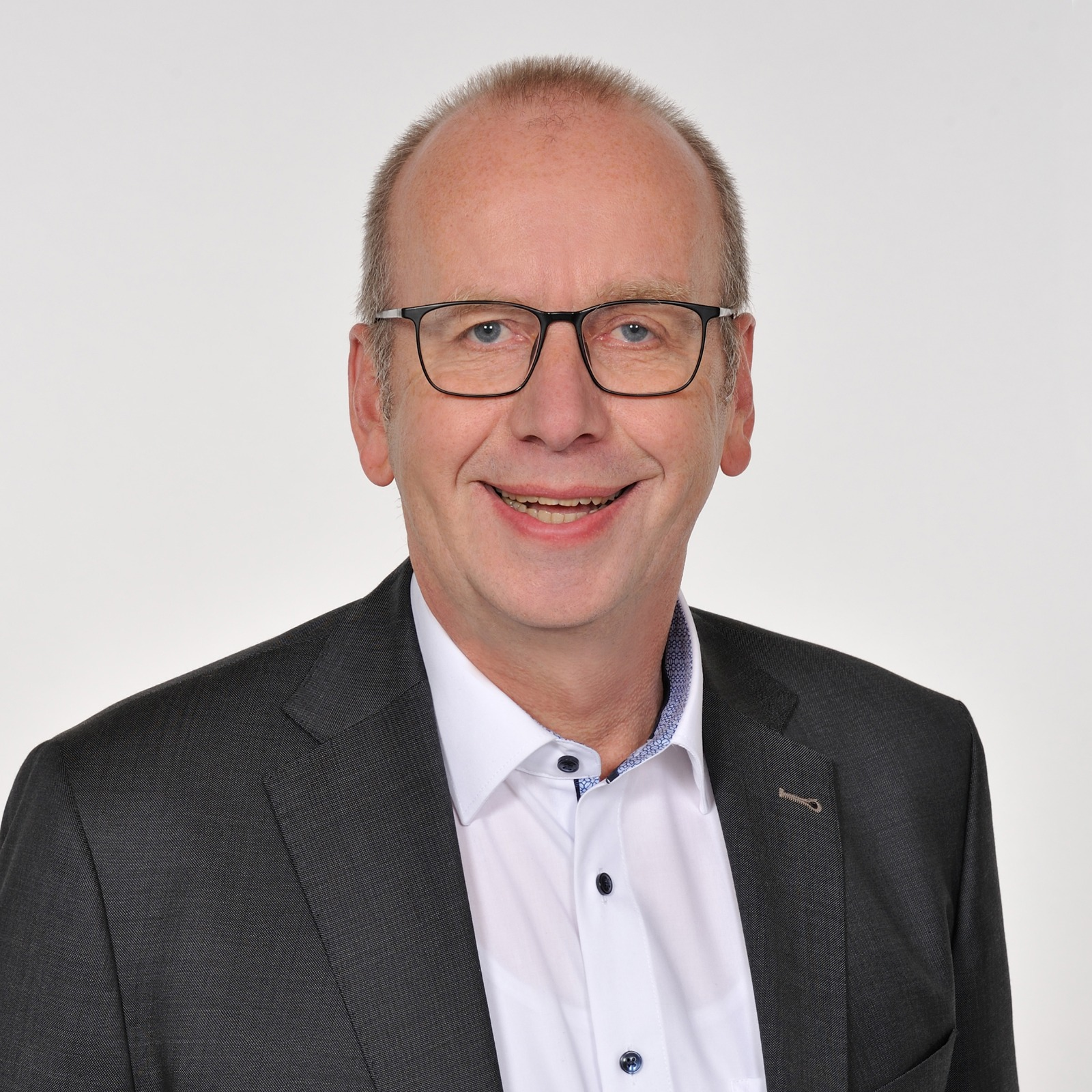 Clemens Poppe lächelnd im dunklen Sakko vor einem hellen Hintergrund.