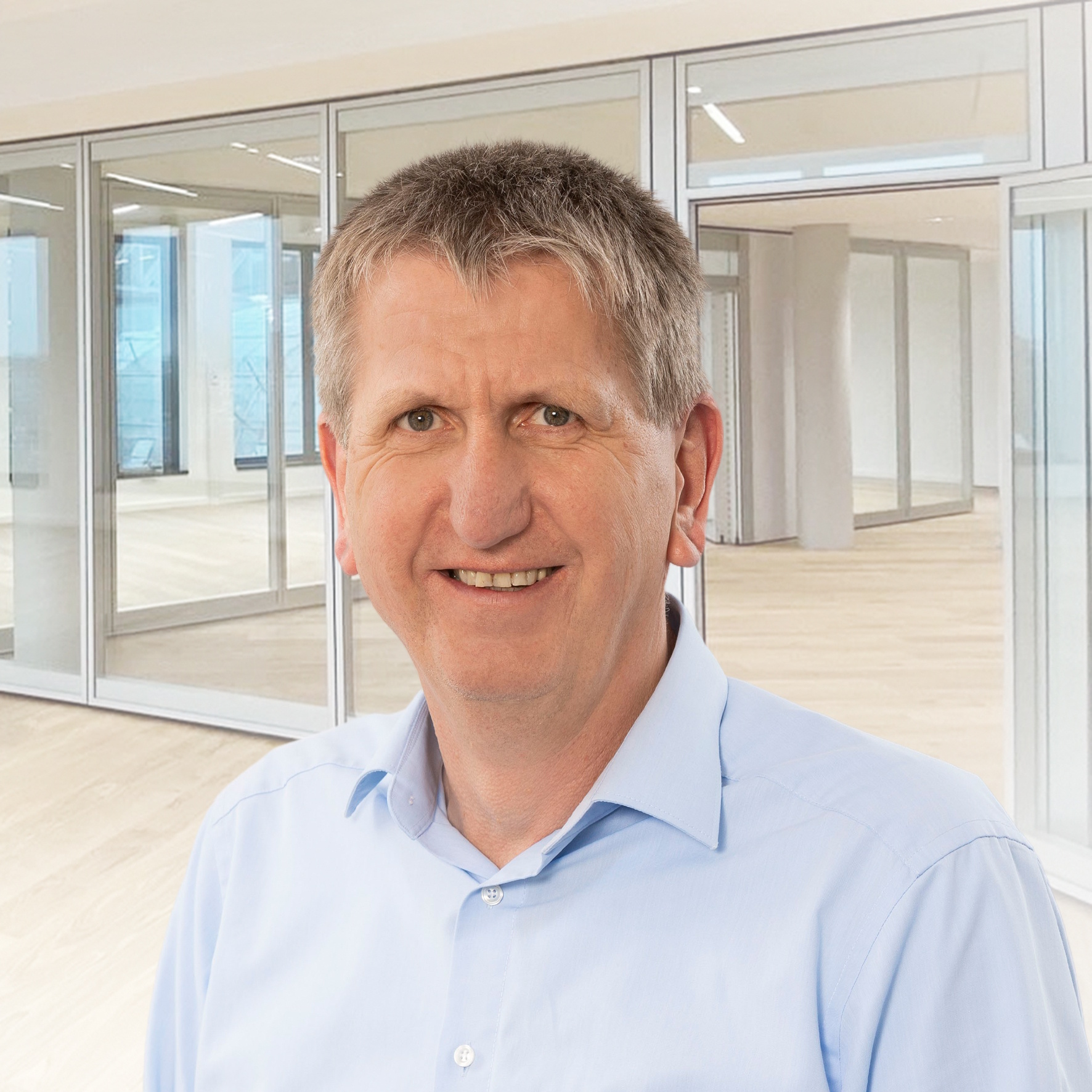 Uwe Behrens im hellblauen Hemd vor einem hellen Bürohintergrund.