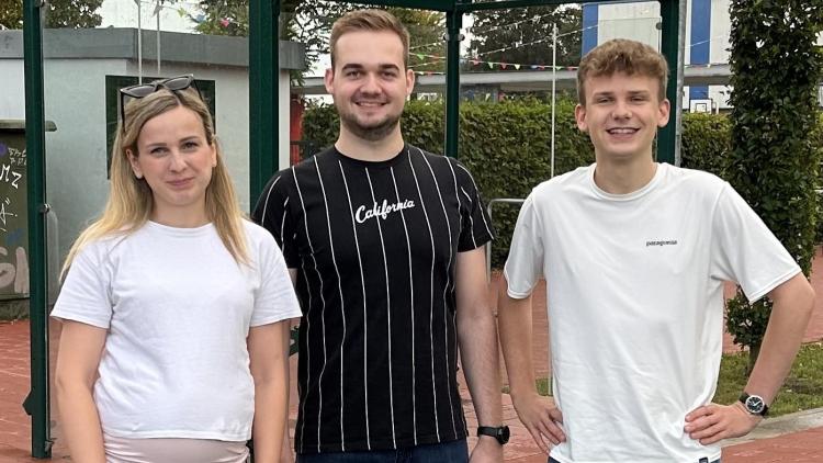 Carolin Abeln, Oliver Renze und Paul Lanwer stehen vor einer Bushaltestelle einer Schule