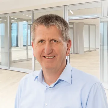 Uwe Behrens im hellblauen Hemd vor einem hellen Bürohintergrund.